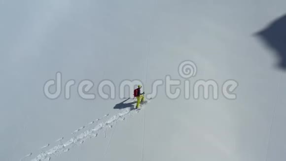 一座大山覆盖着新鲜的雪一个穿着滑雪板的人正在攀登它空中镜头视频的预览图