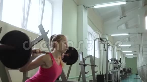 一个年轻漂亮的女孩在健身房里用杠铃做蹲操在健身房训练视频的预览图