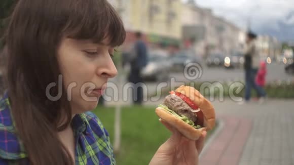 一个女人在一条繁忙的马路旁边咬着一个汉堡的画像慢吞吞的视频的预览图