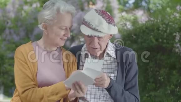 肖像成年男女看旧照片回忆坐在公园长凳上的快乐时刻成熟的夫妇视频的预览图