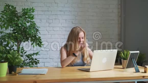 快乐的女人兴奋地看着坐在工作场所的笔记本电脑屏幕庆祝商业成功在获胜视频的预览图