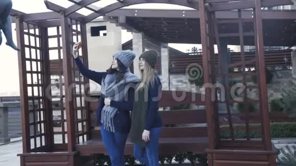 两个戴着帽子戴着围巾的漂亮女孩在院子里自拍视频的预览图