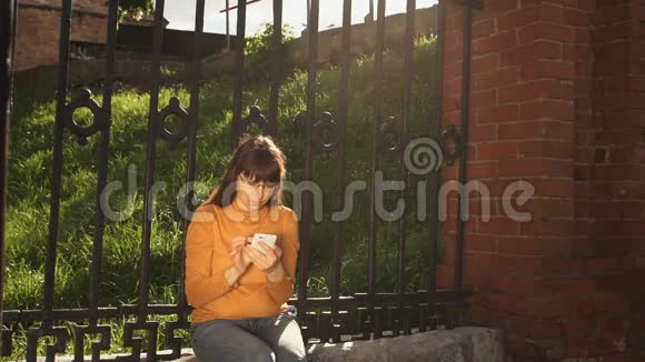 夏天一个年轻的女人在铁栅栏附近的街道上用电话视频的预览图
