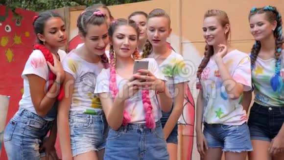 成群结队的女孩带着鲜艳的辫子张开双臂拥抱着小玩意欢笑的年轻人看着手机上的照片视频的预览图