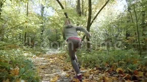 那个金发女孩正在穿过秋天的公园跑步者开始在公园里跑步慢动作视频的预览图