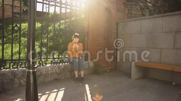 日落时分一位年轻女子在街边的铸铁栅栏旁吃汉堡视频的预览图