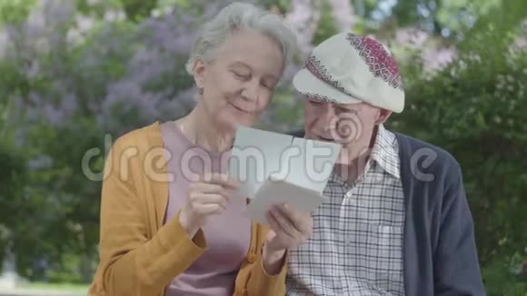 成年男女看着老照片回忆着坐在公园长凳上的快乐时刻成熟的情侣相爱视频的预览图