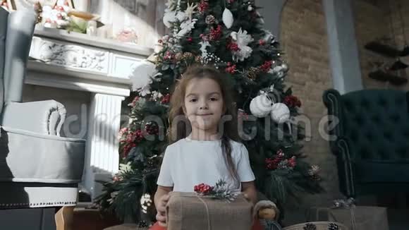 小女孩笑着坐在圣诞树旁边把圣诞礼物放在盒子里视频的预览图