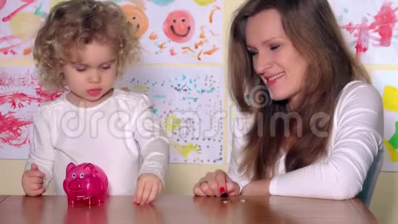 女人带着孩子把硬币放在储蓄罐里用手指看镜头视频的预览图
