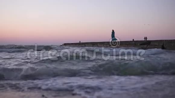 黎明时分一个穿着飘舞衣服的年轻女孩在海上码头漫步迎着冉冉升起的海面孤独的剪影视频的预览图