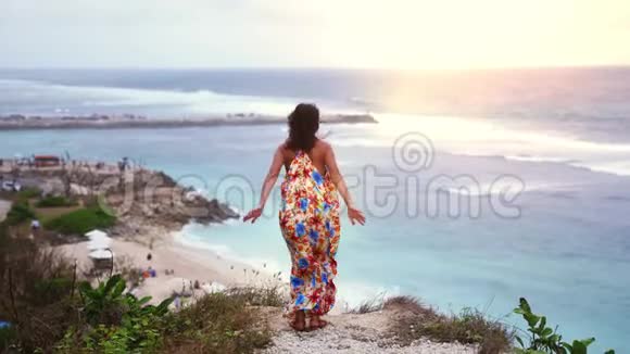 夕阳西下年轻的黑发女人穿着长裙在海边的岩石上跳跃慢动作3840x2160视频的预览图
