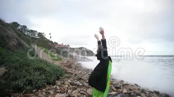 穿着黑色衣服的女人从海里跑出来溅起水花笑了起来多云风天气视频的预览图