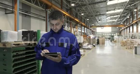 一个男人正在一家工厂工作手里拿着一块数码平板电脑他穿着一身蓝色制服工厂工人视频的预览图