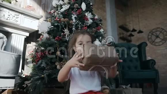 一个留着长发的漂亮小女孩坐在客厅里壁炉靠近圣诞树手里拿着一个视频的预览图