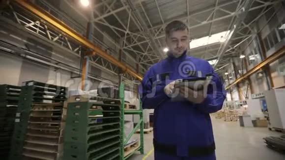 一个男人正在一家工厂工作手里拿着一块数码平板电脑他穿着一身蓝色制服工厂工人视频的预览图
