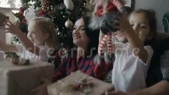 幸福的家庭在家里庆祝圣诞节年轻的一家人坐在圣诞树旁边的地板上兴高采烈视频的预览图