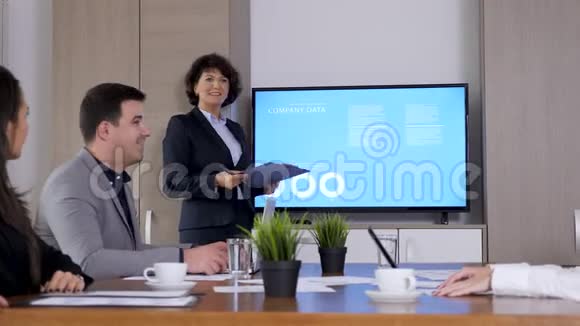 大屏幕电视前会议室的女商人视频的预览图