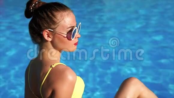 一位年轻女子穿着泳衣坐在游泳池和日光浴旁视频的预览图