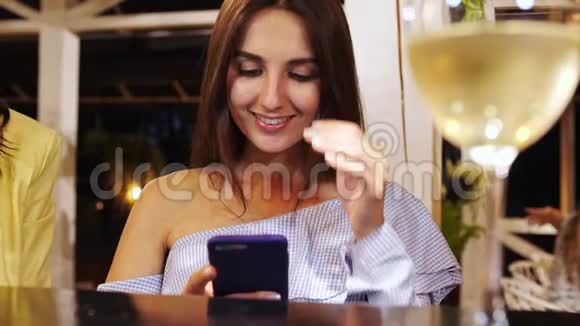 一位年轻漂亮的女孩坐在酒吧里浏览智能手机视频的预览图