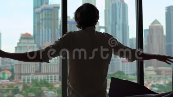一位成功的富人的剪影打开了一扇窗户的窗帘俯瞰着市中心摩天大楼林立视频的预览图