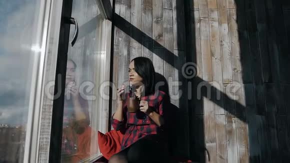 美丽的少女坐在窗前阳光明媚的冬日里手里拿着一杯热茶视频的预览图