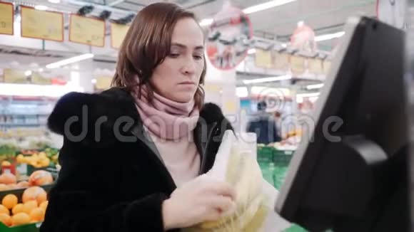 超市里的一个女人在秤上秤香蕉一个穿毛皮大衣的漂亮女人在自助服务中买香蕉视频的预览图