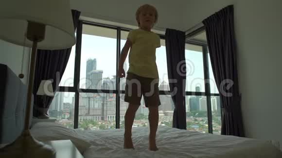 一个小男孩在床上跳跃的慢镜头床垫和枕头概念视频的预览图