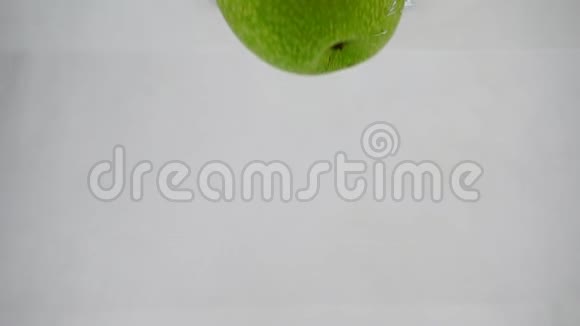 一个绿苹果以缓慢的速度掉进水中有气泡苹果在孤立的白色背景上视频的预览图
