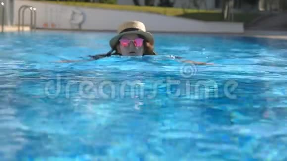 暑假期间戴太阳镜和帽子在游泳池游泳的女性肖像年轻漂亮的女孩在盆里放松视频的预览图