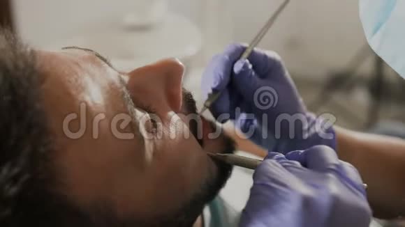 女性牙医用口腔镜和牙科挖掘机检查病人的牙齿他脸上的特写镜头视频的预览图