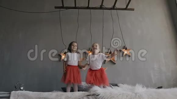 两个小女孩高兴地跳到床上手里拿着礼物的盒子一起过寒假玩得开心视频的预览图