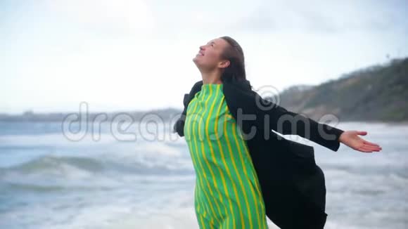 动机射击快乐的女人微笑着举起双手在天空中看着海滩上的海洋和天空视频的预览图