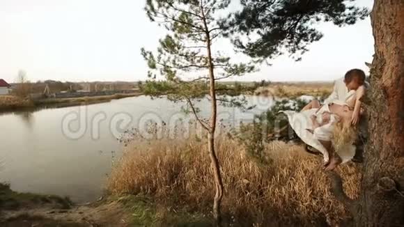 幸福的夫妇正坐在河边的树上漂亮的女人躺在男人的腿上视频的预览图