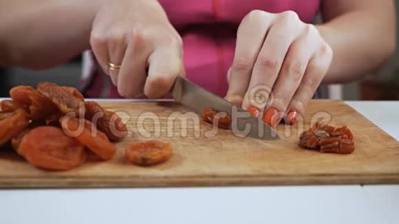 一位年轻的家庭主妇用一把刀在砧板上切果干杏子健康饮食观念视频的预览图