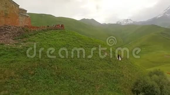 幸福的新娘和新郎在群山和古老的教堂的背景下格鲁吉亚空中景色视频的预览图