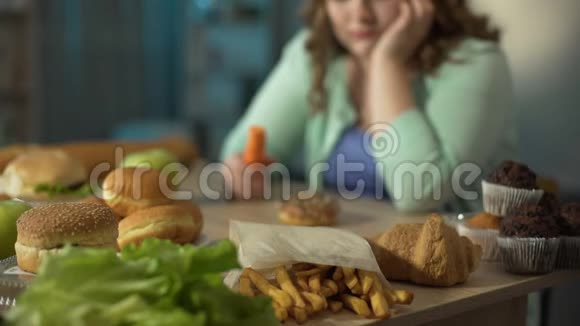 伤心超重的女孩吃胡萝卜看甜甜圈和快餐节食视频的预览图