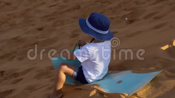 小男孩骑着雪橇在红色的沙漠中滑下沙丘视频的预览图