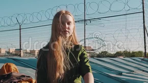 一个长头发的姜黄色漂亮女孩穿着绿色连衣裙坐在屋顶上用倒钩铁丝做屋顶视频的预览图