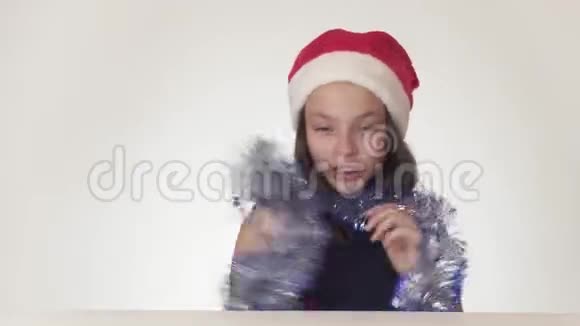 戴着圣诞老人帽子戴着新年礼物的美丽少女在白色的背景下快乐地调皮地跳舞视频的预览图