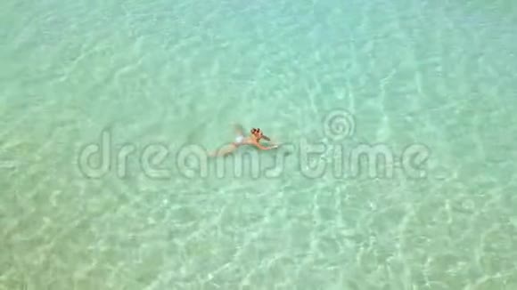 美丽的女人游泳在晶莹剔透的海水无人机从上面看女人沐浴在绿松石的海水中视频的预览图