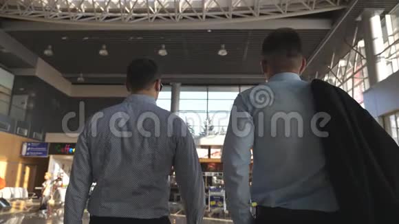 两个年轻的商人在机场候机楼里散步在商业中心的人后方视野慢动作视频的预览图