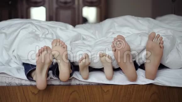幸福的家庭躲在毯子下一起在床上玩耍父母和儿子一起度过空闲时间视频的预览图