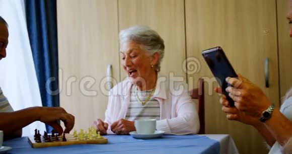 一位年长的女士使用数码平板电脑而她的朋友正在下棋视频的预览图