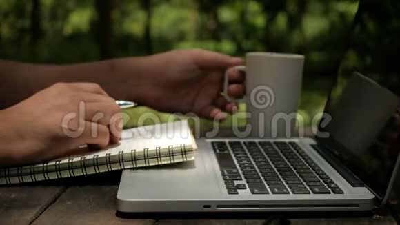一个自由职业者设计师使用笔记本电脑写在笔记本上在花园里喝咖啡视频的预览图