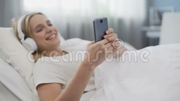 早上在床上十几岁的女孩戴着耳机在网络上交流视频的预览图