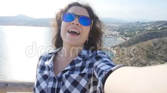 戴墨镜的快乐女旅行者可以在海景中自拍视频的预览图