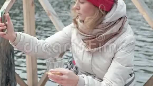 一位女游客穿着温暖的衣服在河岸附近的一座桥上背着一个背包上面铺着地毯喝着热茶视频的预览图