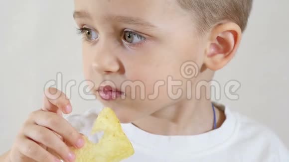 小男孩吃薯片坐在一张白色背景的桌子上特写视频的预览图