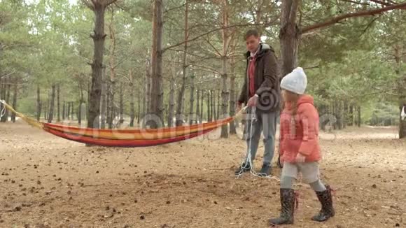 一个在树林里放吊床的年轻人女儿在附近散步视频的预览图