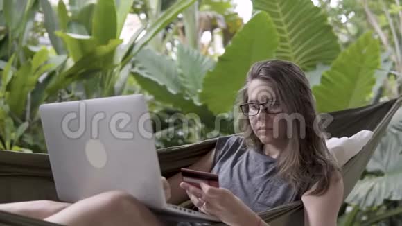女人用信用卡和笔记本电脑成功付款坐在吊床上视频的预览图